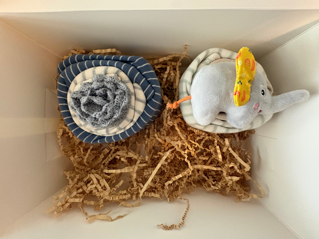 Second cupcake in box is two long sleeved onesies that are stripped white and blue and other is white with gray strips. Two wash gray wash cloths