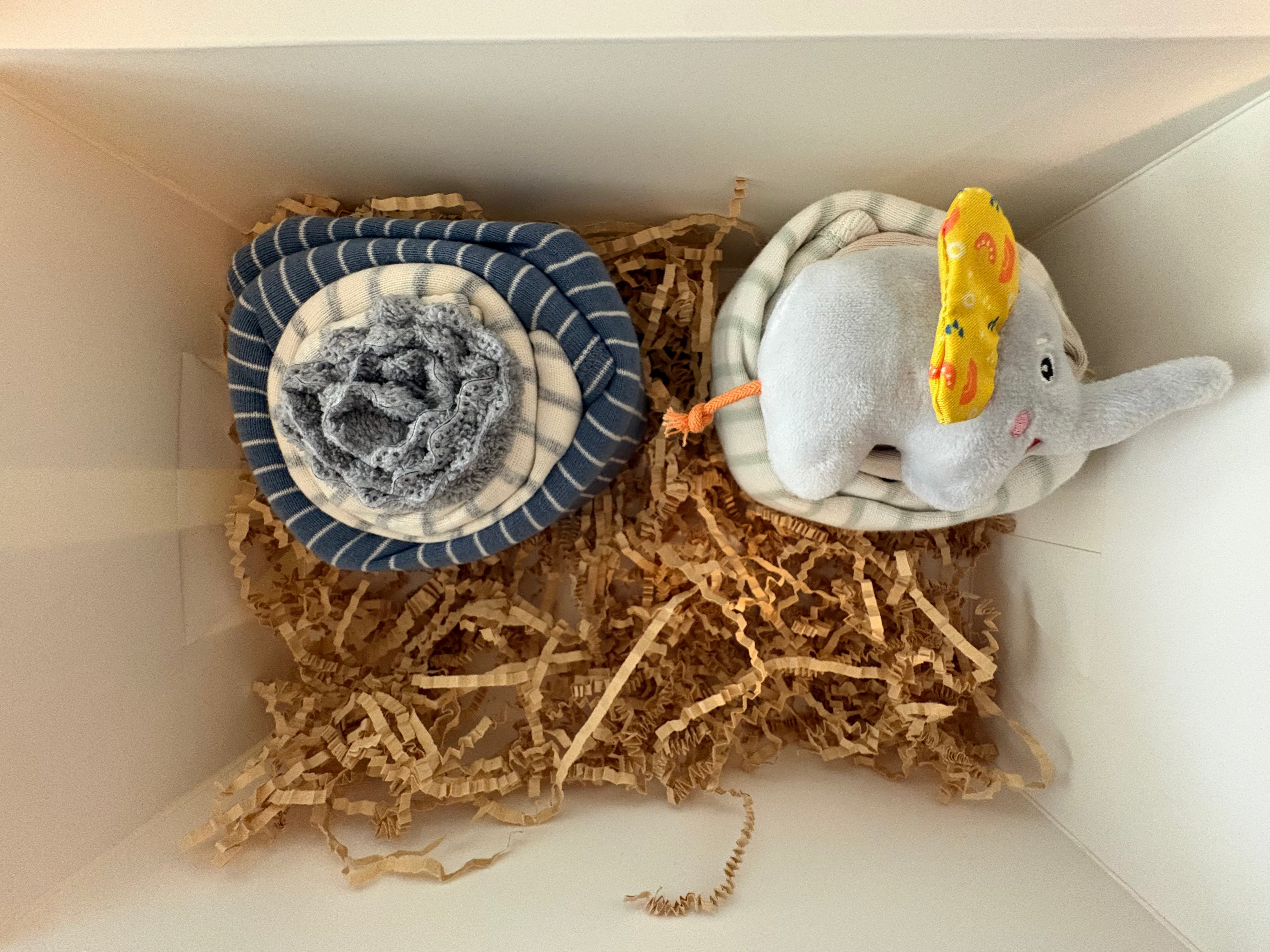 Second cupcake in box is two long sleeved onesies that are stripped white and blue and other is white with gray strips. Two wash gray wash cloths